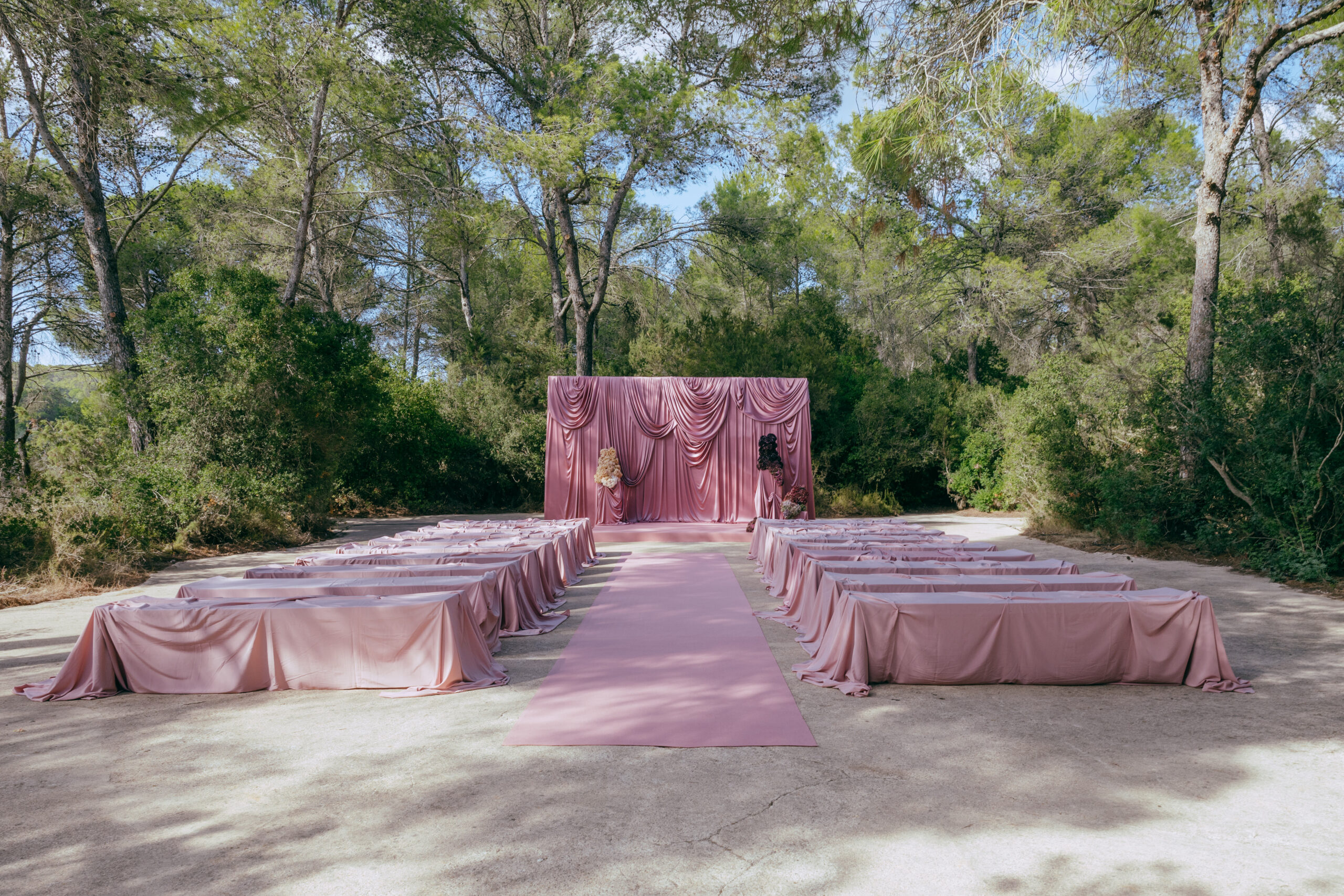 Dusty pink draped ceremony backdrop with sculptural hydrangea florals at a Ca Na Xica wedding in Ibiza.
